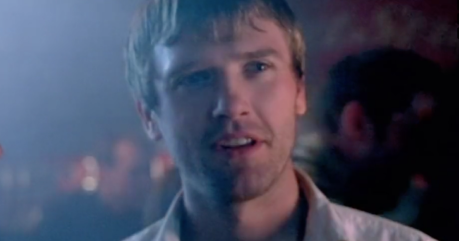 Man with short hair and a surprised expression in a dimly lit bar environment.